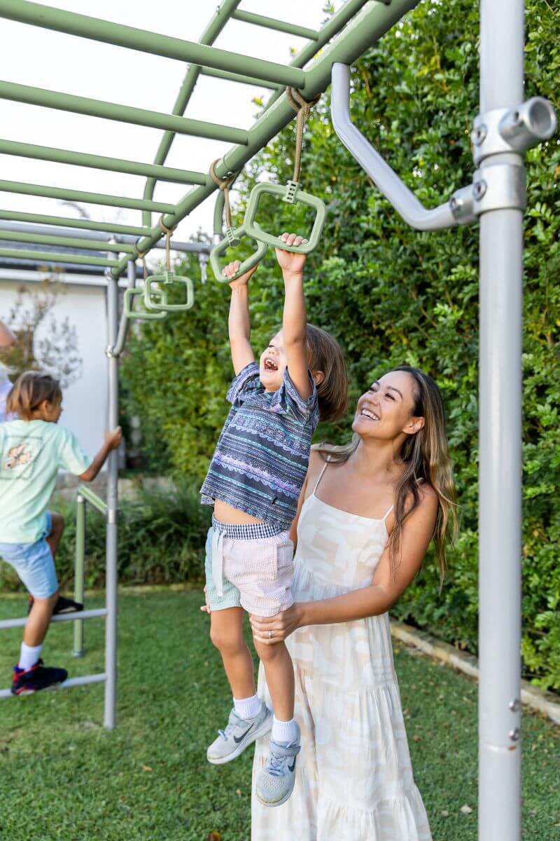 A parent lifting a small child up to the monkey bars for the first time